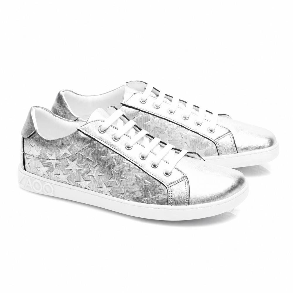 Tenisky SLOQ Stars Silver od ZAQQ majú biele šnúrky a hviezdny vzor na bokoch, doplnené bielou podrážkou s VAOO reliéfom na päte. Tieto topánky sa vyznačujú štíhlym a moderným dizajnom s lesklým kovovým povrchom.