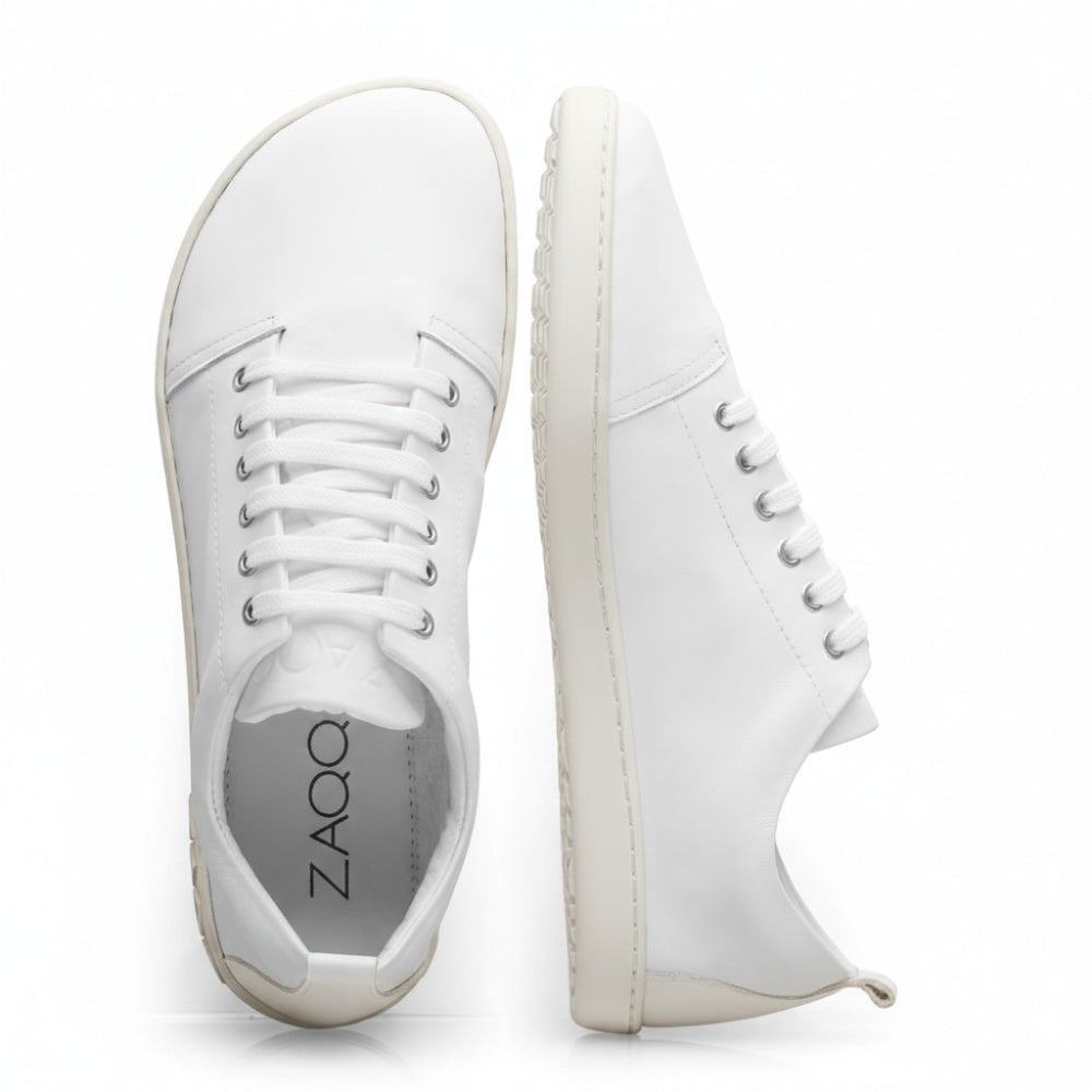 Wir präsentieren den TAQQ Nappa White von ZAQQ: Diese weißen Sneaker sind fachmännisch aus hochwertigem Nappaleder gefertigt und verfügen über klassische Schnürsenkel. Ein Sneaker wird von oben gezeigt, während der andere sein Seitenprofil hervorhebt und das ZAQQ-Branding auf seiner flexiblen Kautschuksohle hervorhebt. Das minimalistische Design steht vor einem schlichten weißen Hintergrund und betont ihre Eleganz.