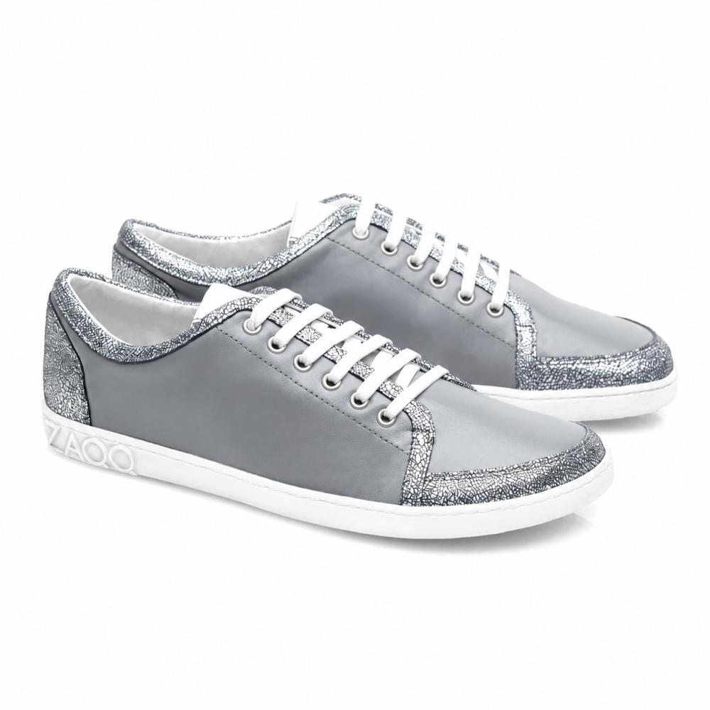 Die TIQQ Grey Silver Sneaker von ZAQQ bestechen durch ihr schlichtes Design aus weichem Nappaleder mit weißen Schnürsenkeln und silbernen Glitzerakzenten, ergänzt durch weiße Sohlen und ein dezentes Logo an der Ferse, und bieten die perfekte Mischung aus Stil und Komfort für jeden Anlass.